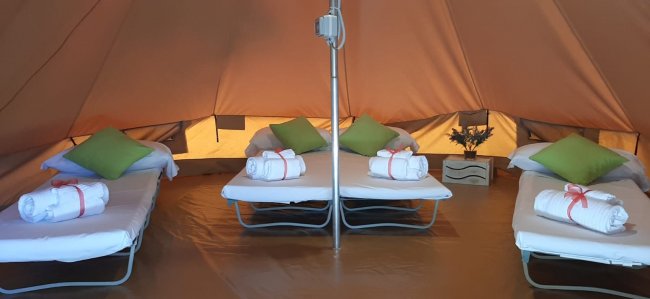 Interno di una tenda con letti e cuscini verdi.
