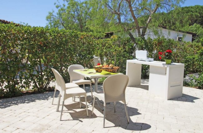 Tavolo e sedie all'aperto con barbecue e piante sullo sfondo.