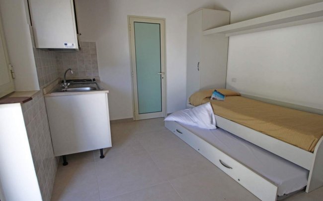 Stanza con letto singolo, angolo cottura e porta bianca.