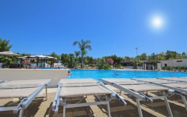 Piscina con sdraio e cielo azzurro.
