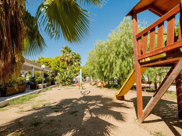 Parco giochi con scivolo, circondato da palme.