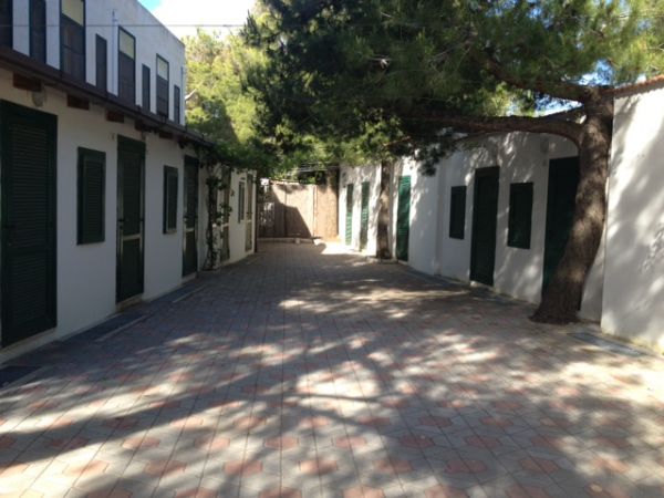 Cortile pavimentato tra edifici bianchi con persiane verdi.