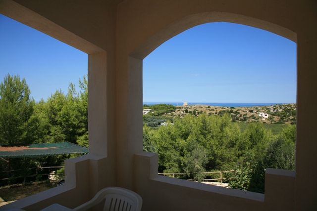 Vista su colline verdi e mare da una terrazza con arco.