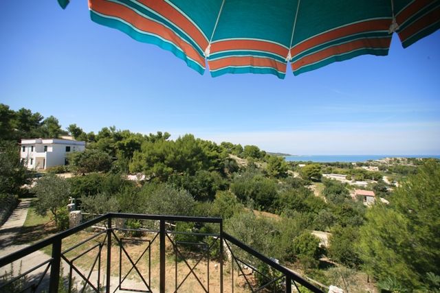 Vista sul mare da una terrazza con ombrellone verde.