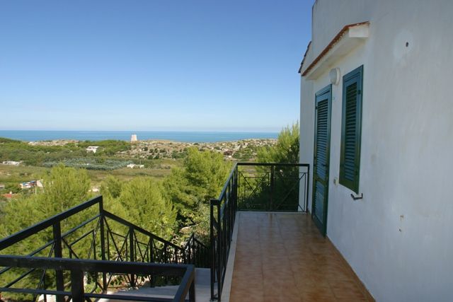 Balcone con vista sul mare e colline verdi.