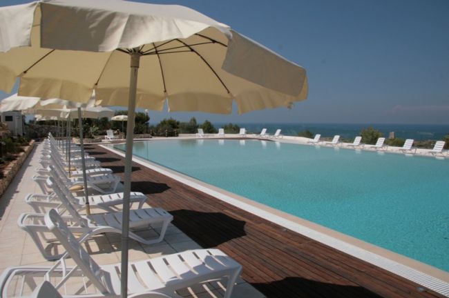 Piscina con ombrelloni e lettini bianchi vicino al mare.
