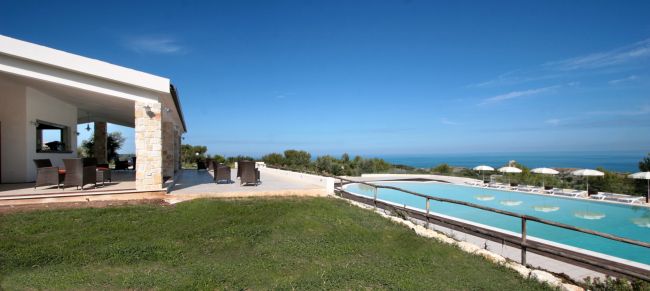Piscina a sfioro con vista sul mare, affiancata da un patio moderno.