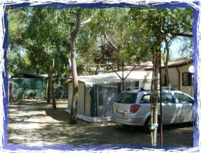 Area campeggio con auto parcheggiata accanto a una tenda e alberi intorno.