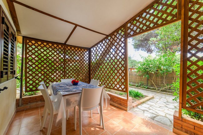 Portico con tavolo e sedie, giardino sullo sfondo.