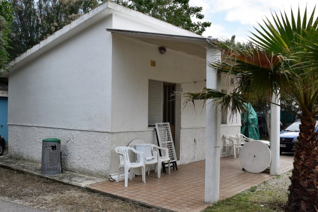 Bungalow bianco con veranda, sedie e palma davanti.