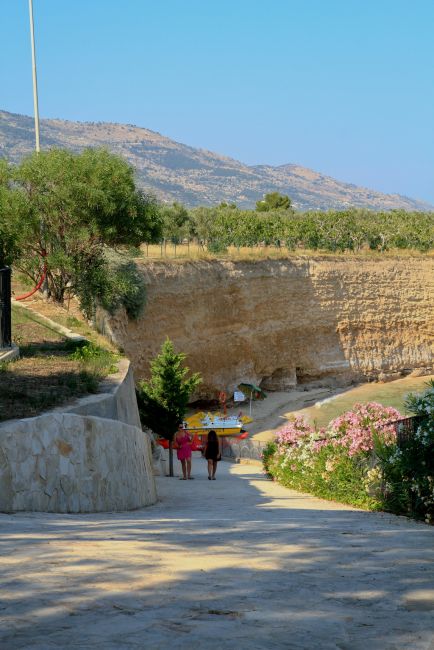 Due persone camminano su un sentiero verso una spiaggia, circondate da colline.