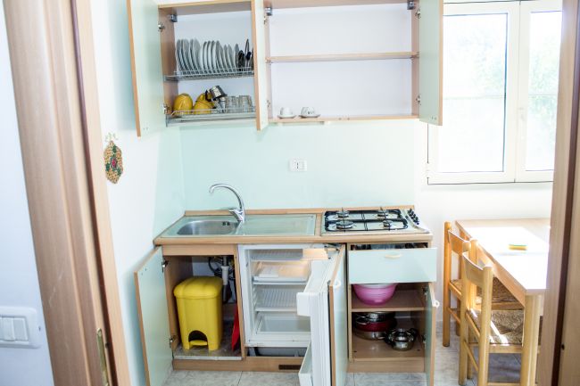 Cucina aperta con scaffali e cassetti aperti, tavolo vicino alla finestra.