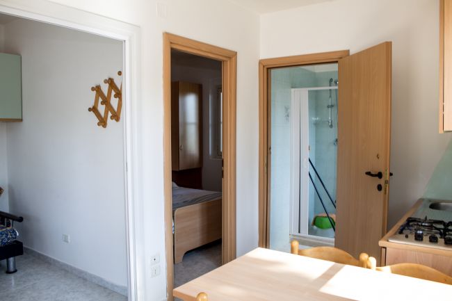 Cucina e corridoio con porte aperte verso una stanza e un bagno.