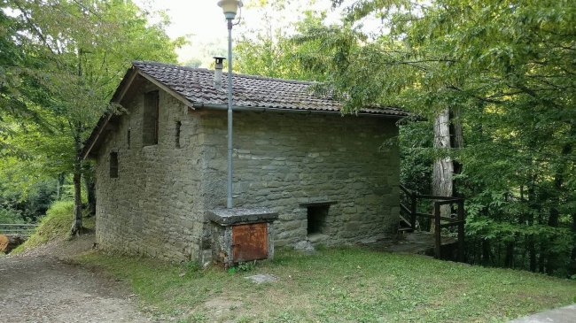Edificio in pietra con tetto spiovente tra alberi.