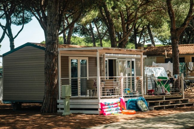 Una casetta in legno in campeggio con veranda e alberi intorno.