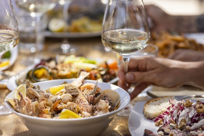 Tavola imbandita con piatti di pesce e bicchieri di vino.