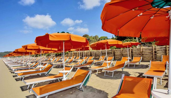Ombrelloni arancioni e lettini su una spiaggia sabbiosa sotto un cielo azzurro.