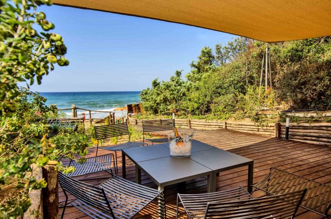 Terrazza con tavolo e sedie vista mare, circondata da vegetazione.