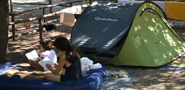 Due persone leggono su un materasso accanto a una tenda verde.
