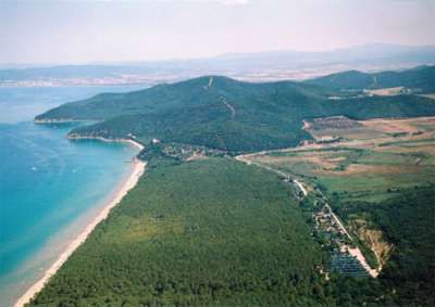 Vista aerea di una costa con spiaggia, foresta e colline sullo sfondo.