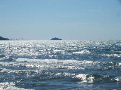 Oceano con onde increspate sotto il sole e un'isola in lontananza.