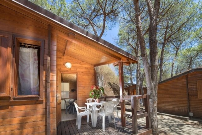 Bungalow di legno con veranda e sedie bianche.