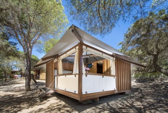 Una tenda di legno e tela tra alberi soleggiati.