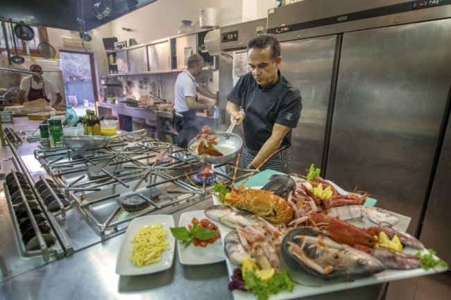 Chef cucina pesce fresco in una cucina industriale.