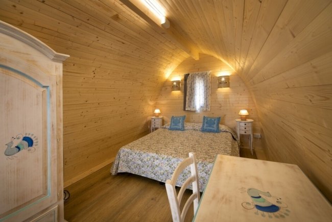 Interno di una camera con pareti in legno, letto matrimoniale.