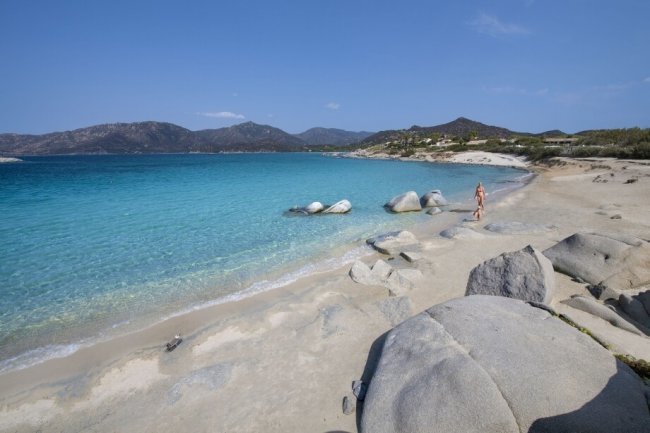 Spiaggia sabbiosa con rocce e mare turchese.