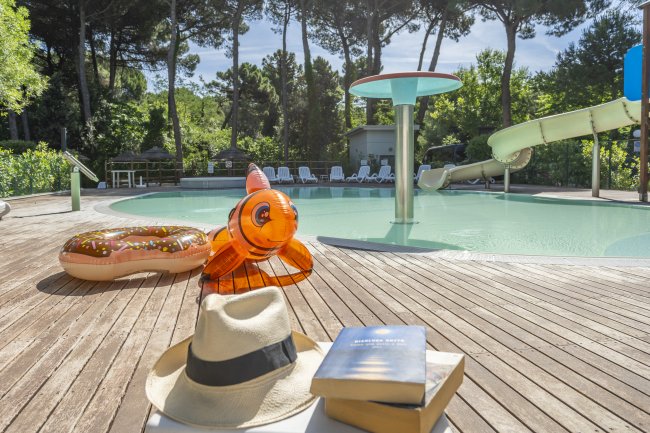 Piscina con ciambella gonfiabile, libro e cappello sul bordo.