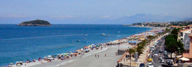 Una lunga spiaggia sabbiosa con ombrelloni colorati, una strada e auto parcheggiate.