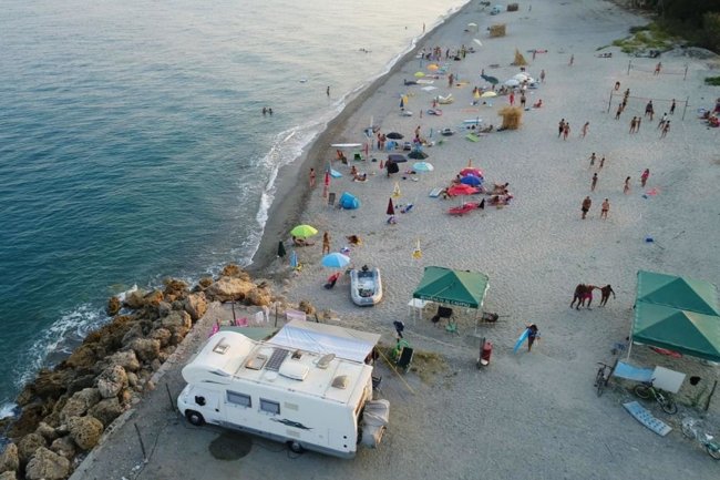 Spiaggia affollata con camper e ombrelloni.