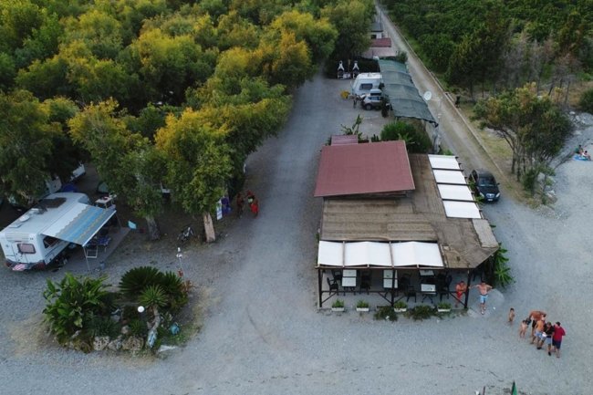 Piazzale con edifici, camper e vegetazione alberata viste dall'alto.