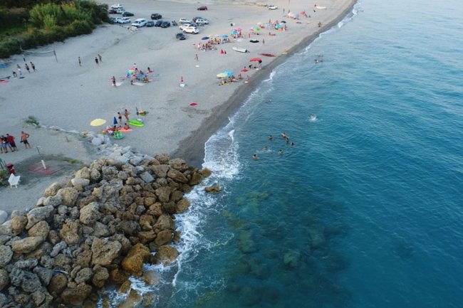 Spiaggia con ombrelloni colorati, bagnanti e mare limpido.