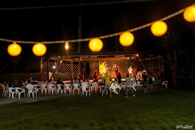 Spettacolo serale all'aperto con pubblico e luci decorative.