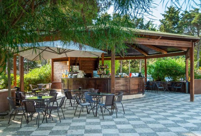 Bar all'aperto con tavoli e ombrellone su pavimento a scacchi.