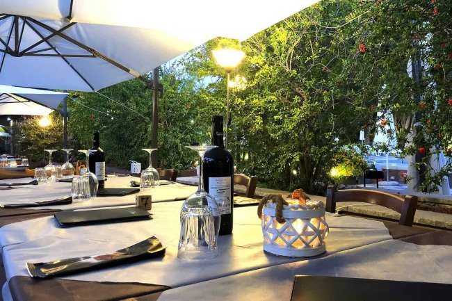 Tavolo apparecchiato all'aperto con bottiglie di vino e bicchieri.