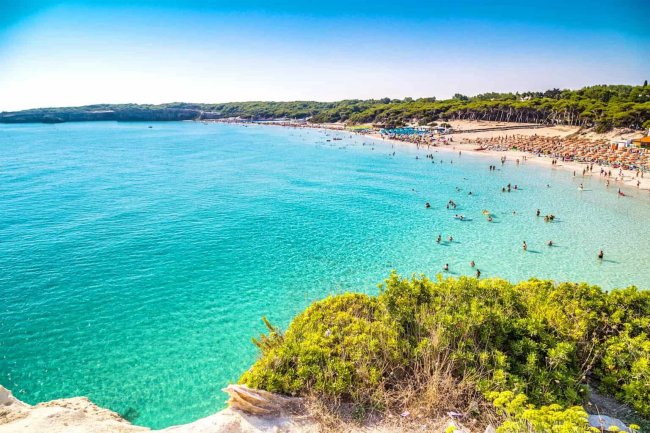 Spiaggia affollata con mare turchese e sabbia chiara.