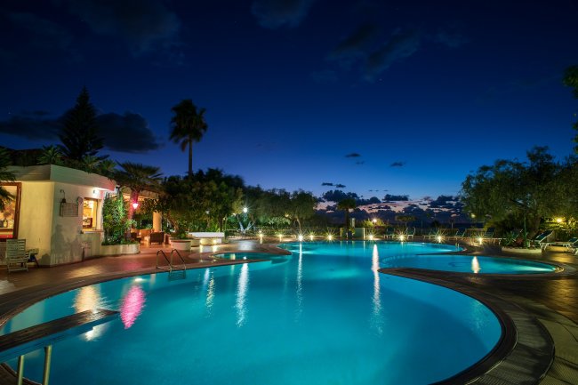 Piscina illuminata di sera con cielo stellato.