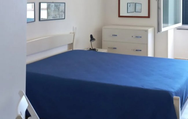 Camera da letto con coperta blu e finestre aperte.