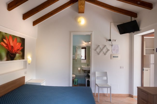 Camera con soffitto a travi, letto e bagno in fondo.