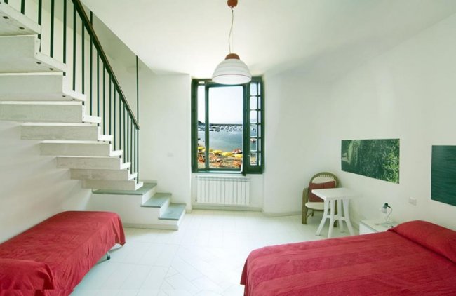 Stanza con due letti rossi, scala, e finestra con vista.