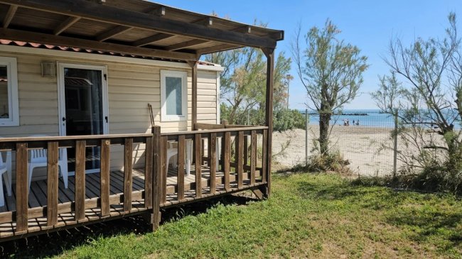Veranda in legno affacciata su spiaggia sabbiosa con vegetazione.