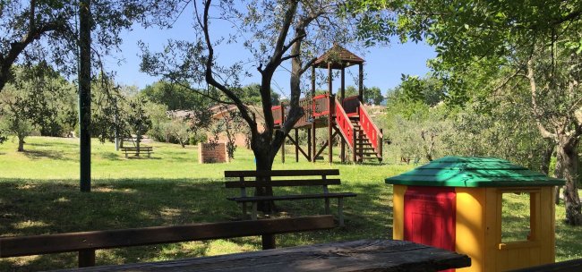 Parco giochi con panchine sotto gli alberi.