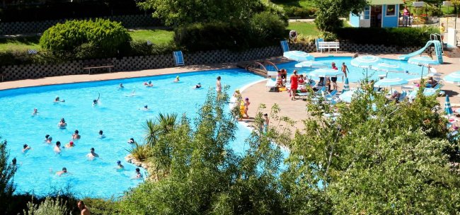 Piscina piena di persone circondata da alberi.