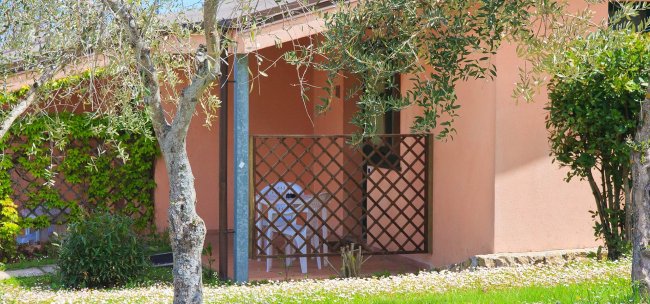 Casa rosa con grata in legno e sedie bianche.