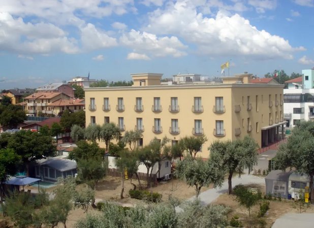 Edificio beige a tre piani, circondato da alberi.