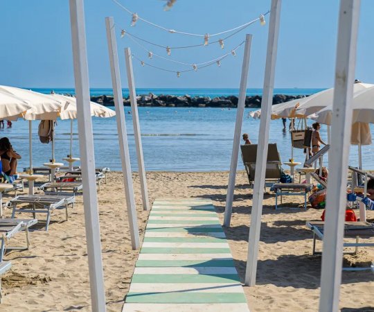 Spiaggia con ombrelloni e lettini, passerella verso il mare.