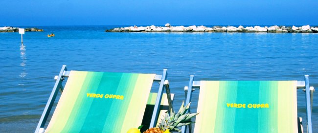 Sedie a sdraio fronte mare con frutta su un tavolino.
